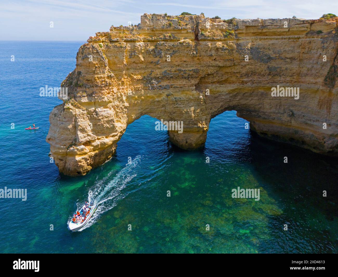 Un grand bateau passe sous des arches naturelles faites de rochers dans l'eau cristalline sur la côte, vue aérienne, Praia da Marinha, double arc rocheux, Lagoa Banque D'Images