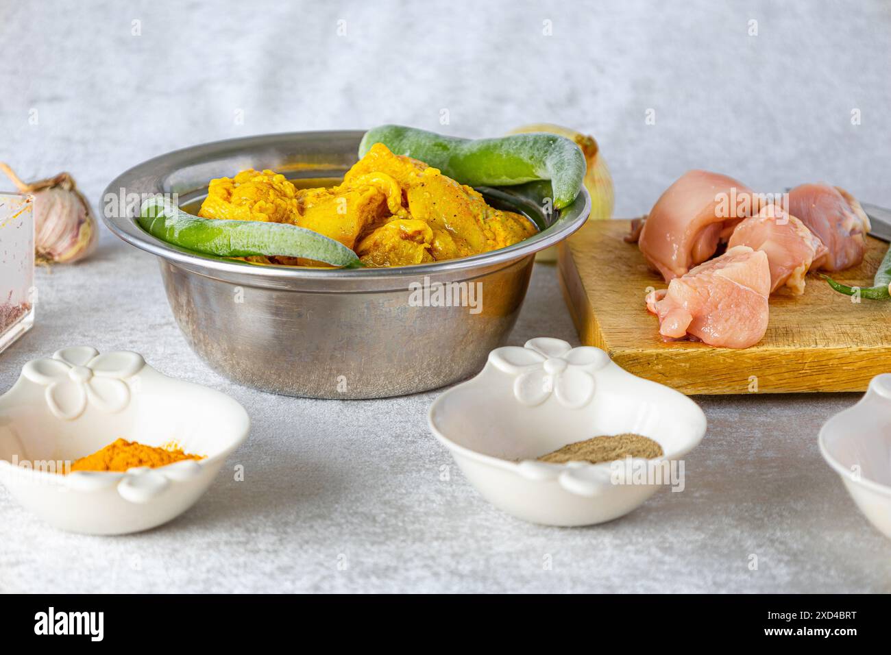 Les ingrédients pour cuire le poulet sur un fond blanc, bol de poulet mariné et piments, planche à découper avec des morceaux de poulet cru sur le dessus Banque D'Images