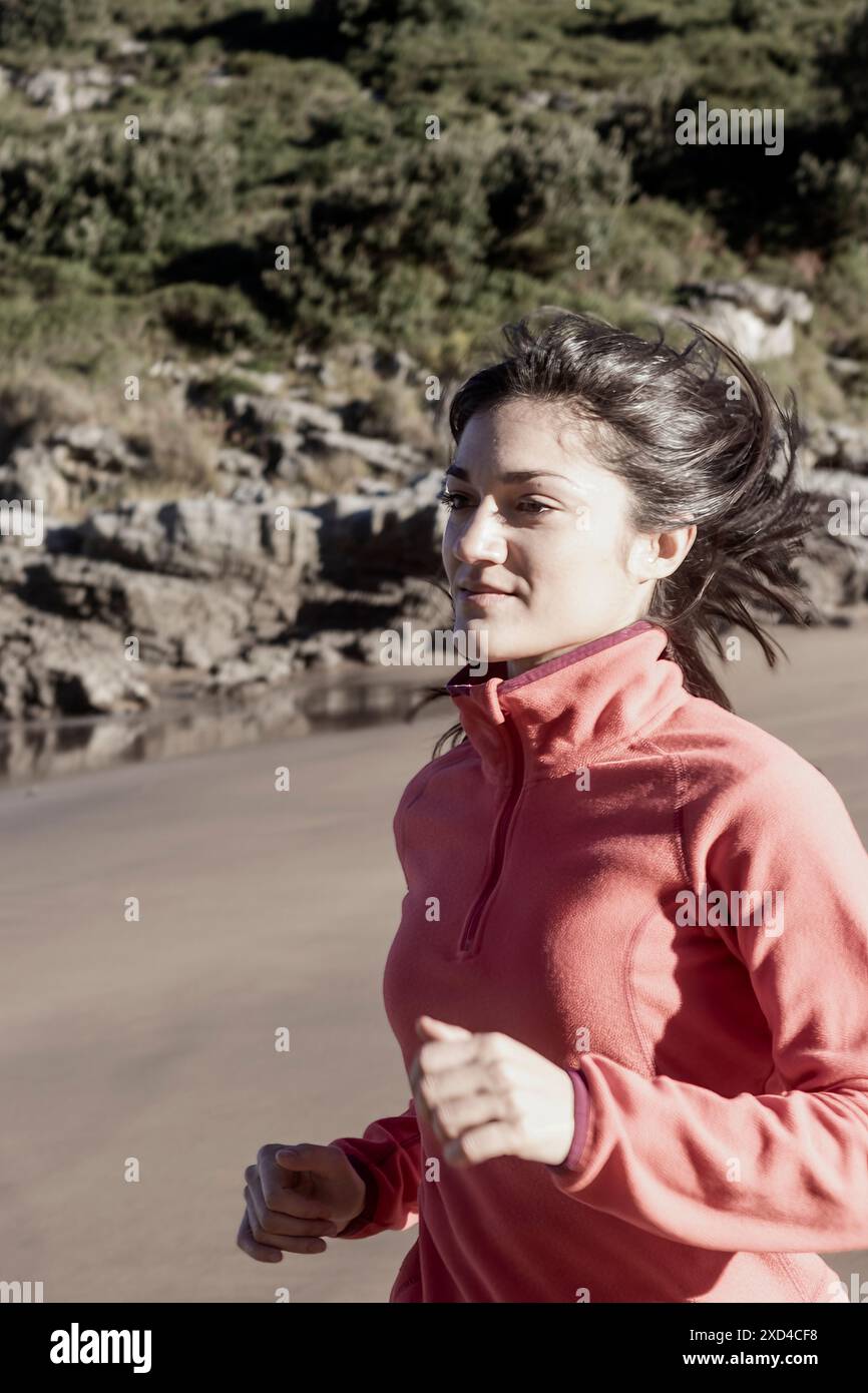 Jeune femme jogging sur la plage portant veste rose.fitness et photographie de style de vie sain. Concept d'exercice et de bien-être Banque D'Images