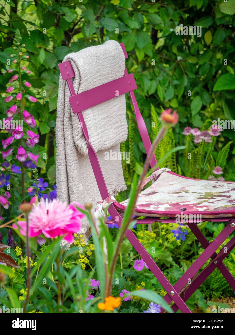 Chaise de jardin en métal mauve avec coussin floral et couverture drapée sur le dos. Banque D'Images