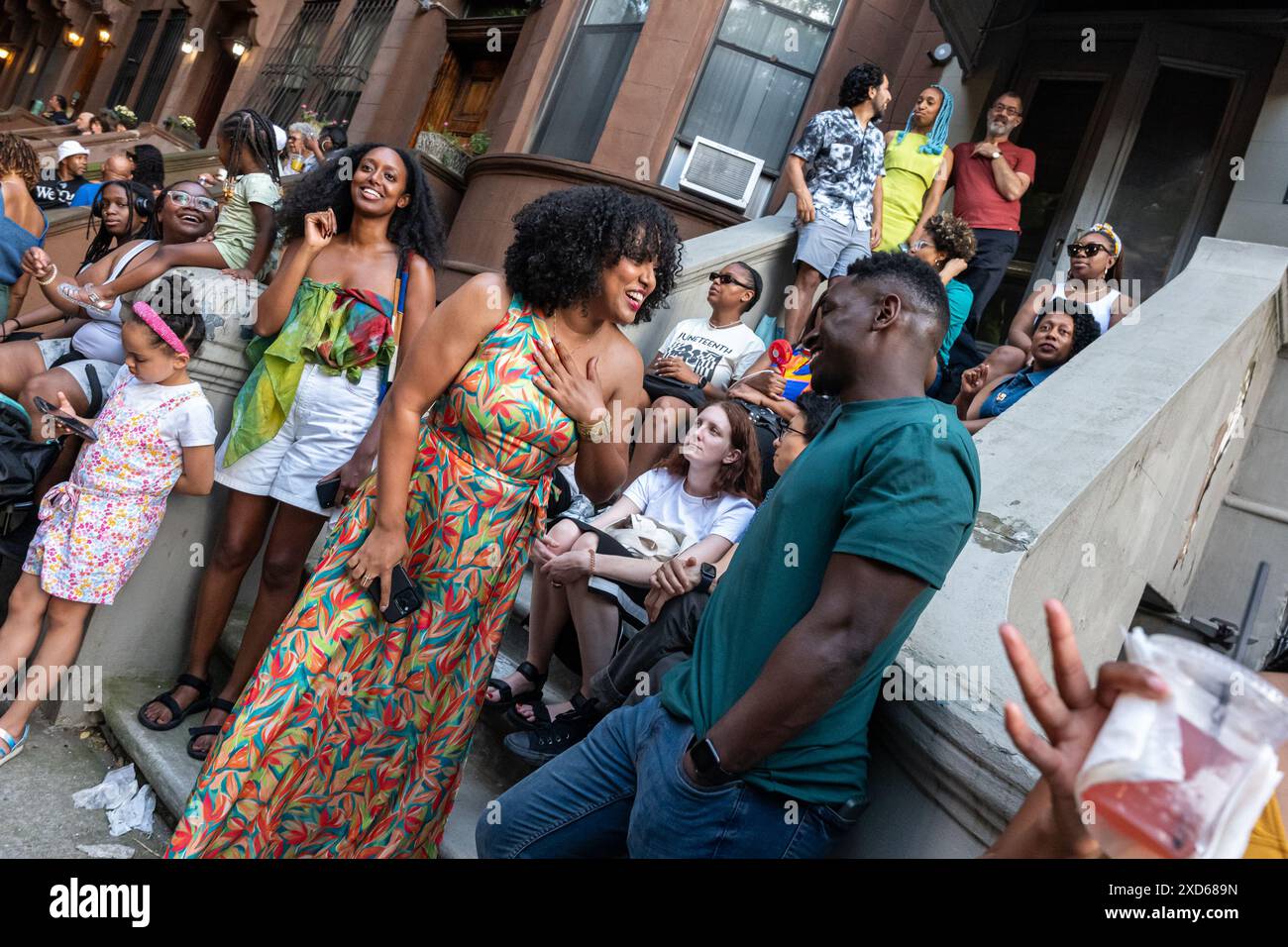 New York, New York, États-Unis. 19 juin 2024. Les voisins se rassemblent sur des stoops pendant les sessions Dance TheSoapBoxPresents Stoop lors d'un concert sur la 119e rue entre Adam Clayton Powell et Malcolm X Blvd avec des danseurs, Big Ban Jubilee un groupe d'orchestre de 12 pièces, lindy hop, musique swing animée par Dandy Wellington à Harlem, New York. Il s'agissait de la 3e célébration annuelle de la Soapbox. L’artiste Maija Abney a commencé les sessions pendant la pandémie pour garder les artistes de la scène frais dans leur travail et «célébrer la journée de la liberté», a-t-elle dit. Les sessions Stoop se poursuivront jusqu'à la fin de l'été Banque D'Images