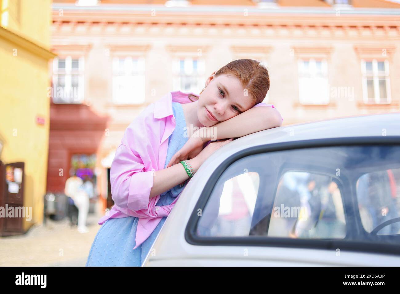 Une fille dans une robe d'été appuyée contre une voiture rétro blanche Banque D'Images