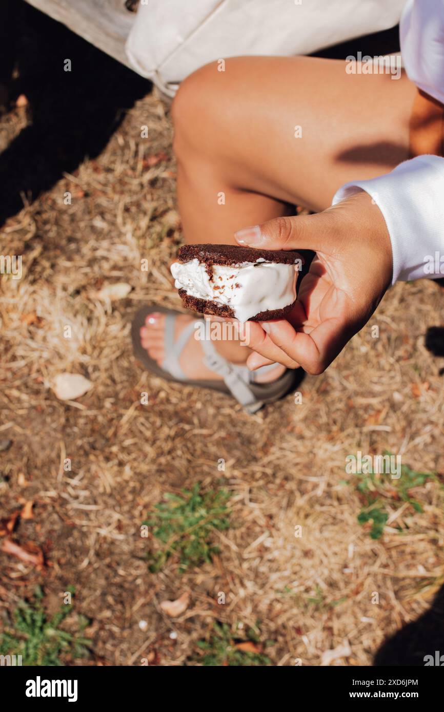 femme profitant d'un sandwich à la crème glacée sur un banc de pique-nique Banque D'Images