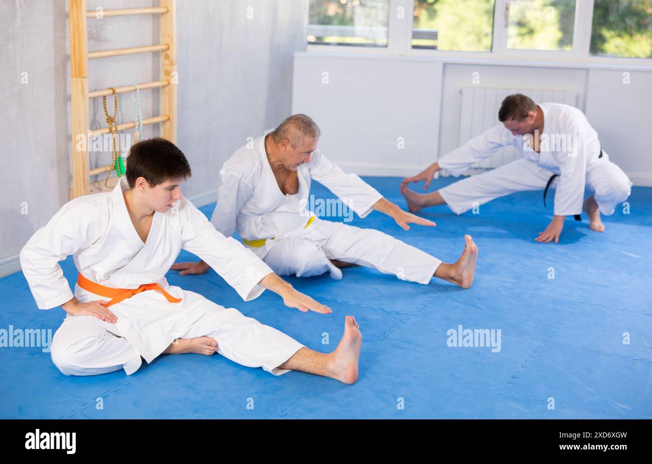 Hommes d'âges différents dans un kimono blanc faisant des étirements musculaires avant l'entraînement de karaté ou de judo Banque D'Images