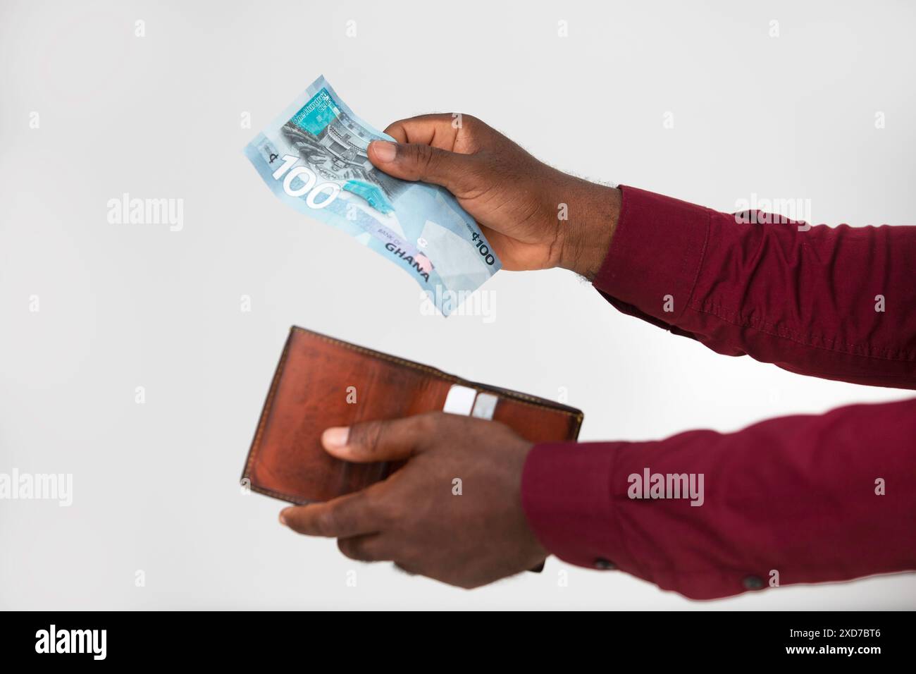 Mains de la personne noire enlevant, mettant une seule cent note cedi ghanéenne dans le portefeuille sur fond blanc, tenant le portefeuille brun Banque D'Images