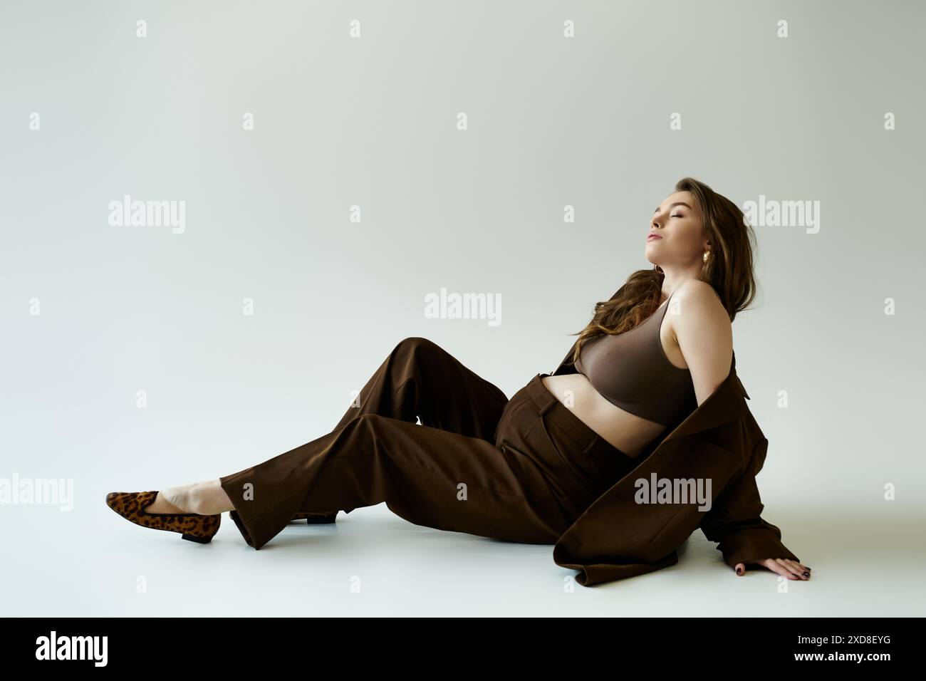 Femme enceinte en haut noir et pantalon brun est élégamment assis sur le sol. Banque D'Images