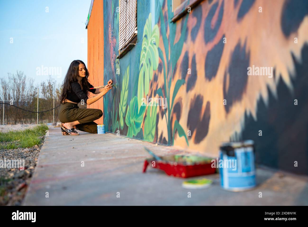 Femme artiste peignant murale colorée sur le mur extérieur à la lumière du jour Banque D'Images