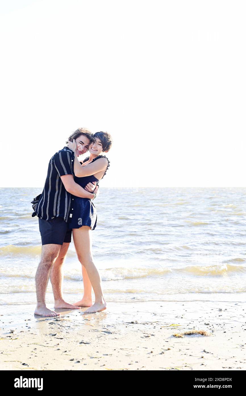 Deux jeunes gens embrassant sur la plage, souriant et appréciant th Banque D'Images