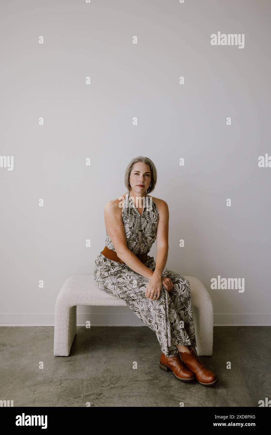 Femme aux cheveux gris assise sur un banc contre un mur blanc Banque D'Images