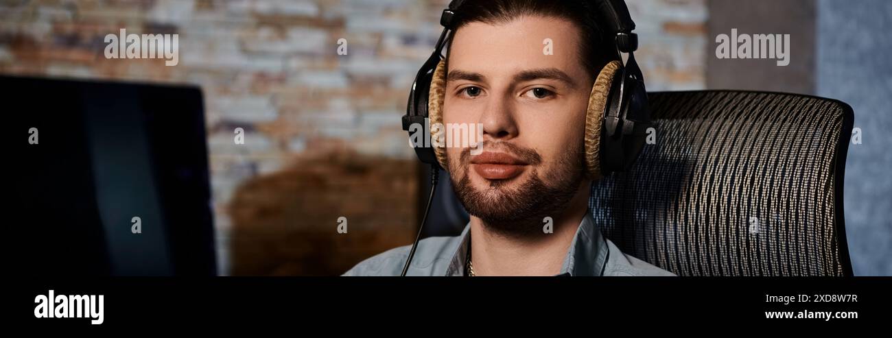 Un homme avec des écouteurs est assis devant un ordinateur dans un studio d'enregistrement, peaufinant la musique pour une répétition de groupe. Banque D'Images