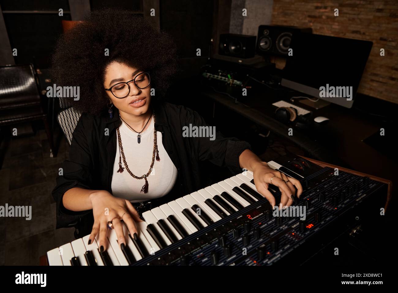 Une femme portant des lunettes joue du clavier dans un studio d'enregistrement pendant une répétition d'un groupe de musique. Banque D'Images