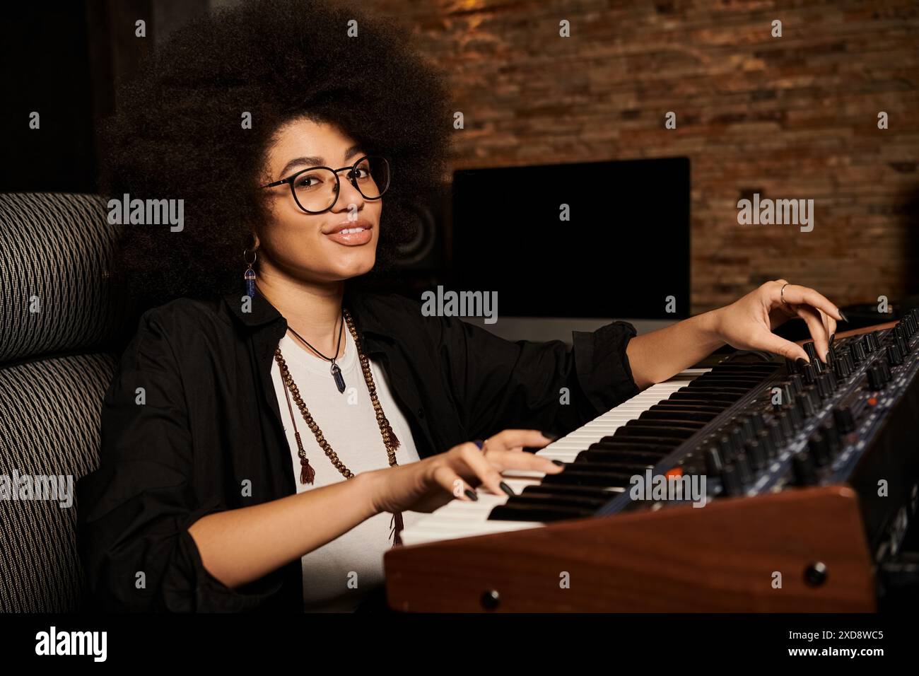 Femme avec des cheveux afro jouant énergiquement un clavier dans un studio d'enregistrement pendant une répétition de groupe de musique. Banque D'Images