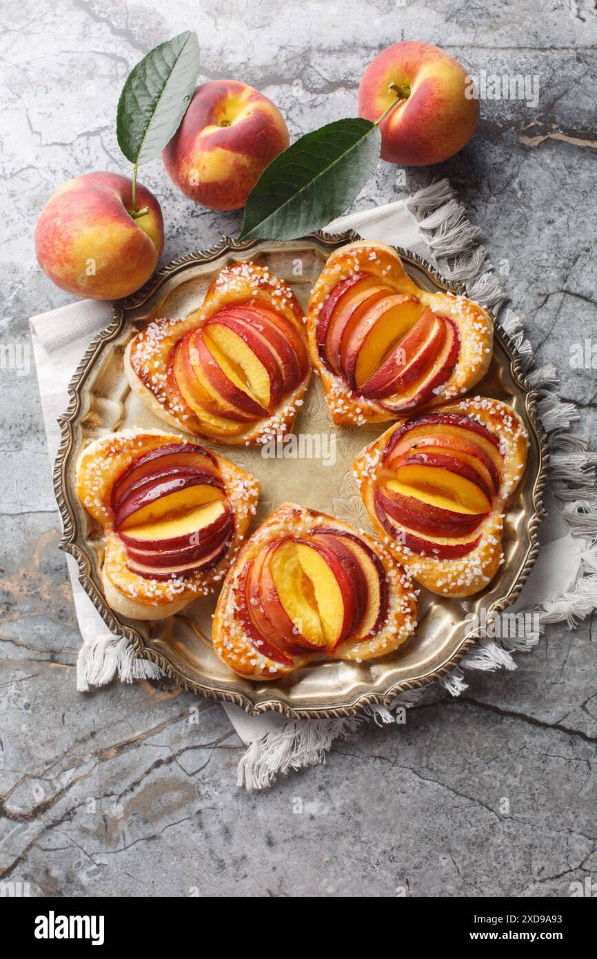 Gâteaux feuilletés à la pêche au four avec des fruits frais et de la confiture gros plan dans une assiette sur la table. Vue de dessus verticale Banque D'Images