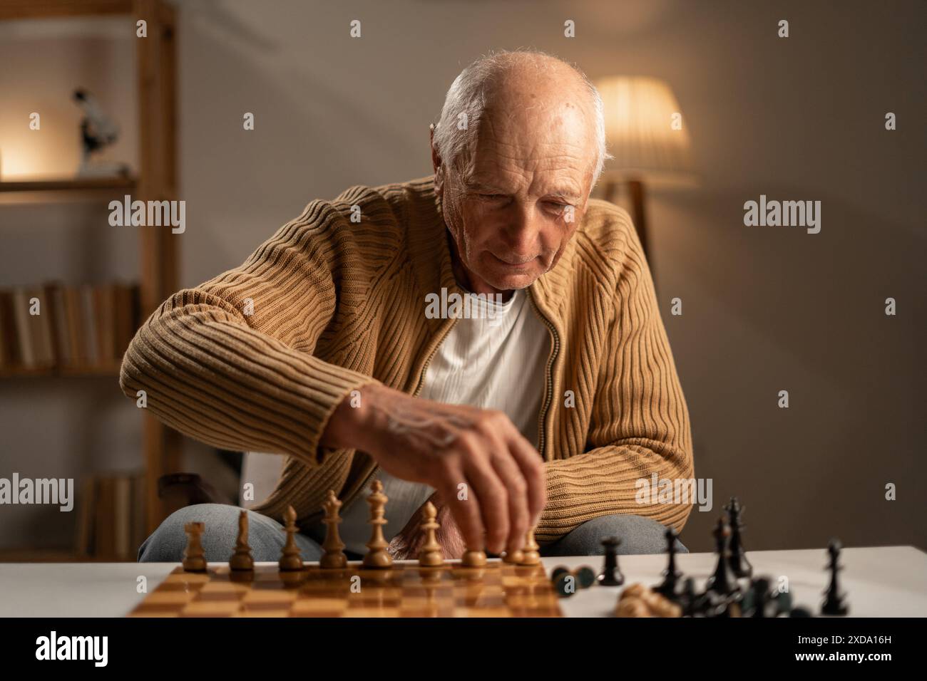 Vieil homme jouant aux échecs seul à table le soir à la maison. Banque D'Images