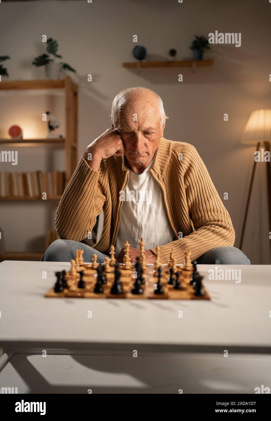 Vieil homme réfléchi regardant les pièces d'échecs assis avec l'échiquier prêt à jouer Banque D'Images
