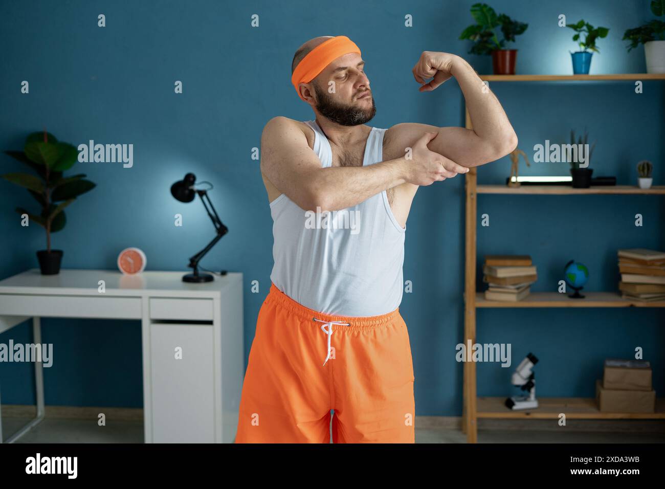 Portrait d'un homme mûr heureux habillé dans le réservoir supérieur montrant des biceps à la salle de gym à la maison Banque D'Images