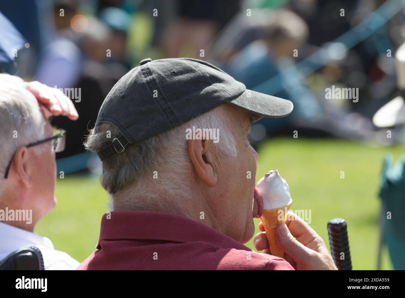 Homme senior portant un chapeau de crête léchant une crème glacée, vue de côté. Banque D'Images