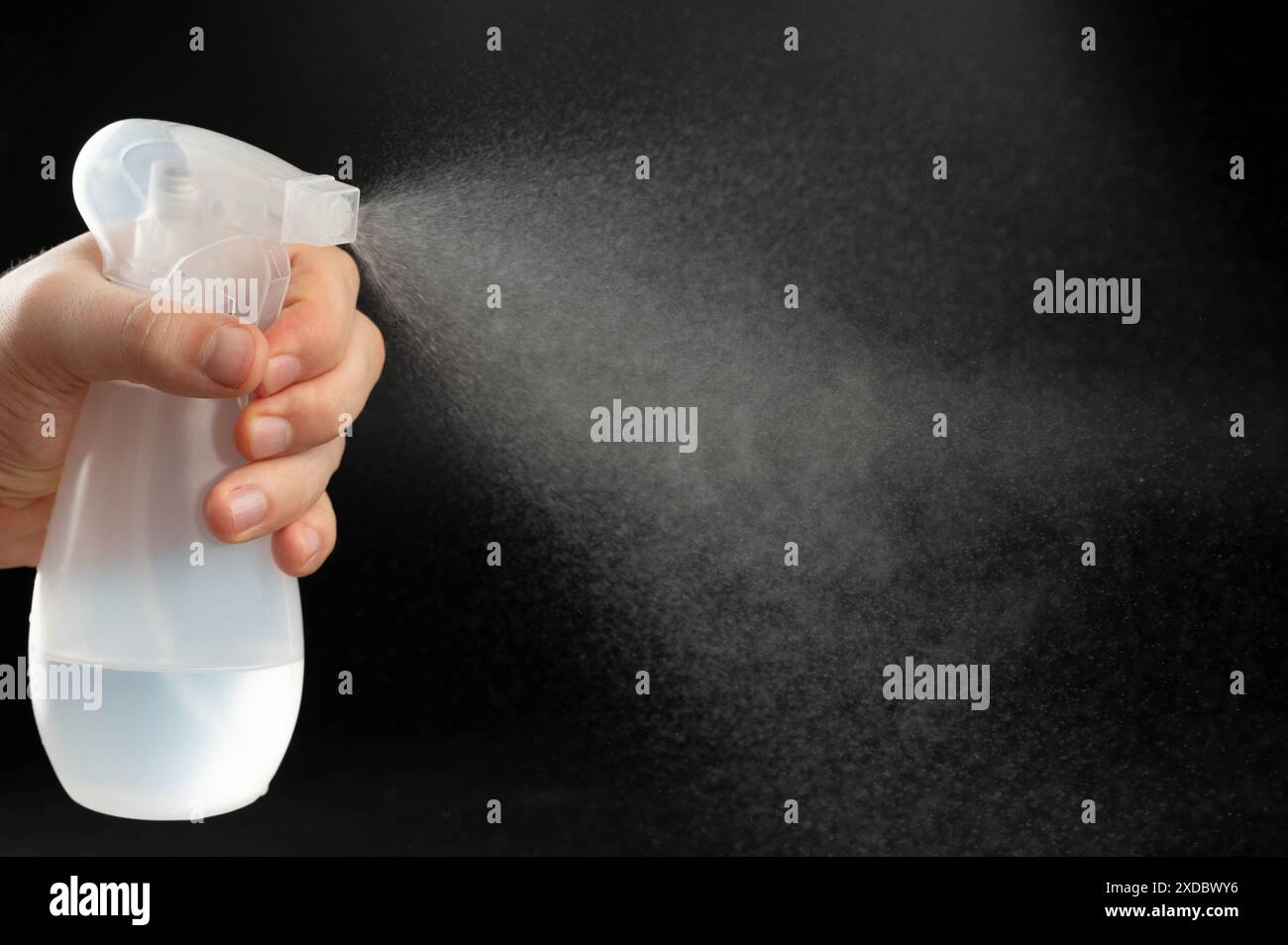 Jet d'eau liquide pulvérisé à partir d'un flacon de pulvérisation en plastique isolé sur fond noir de studio Banque D'Images