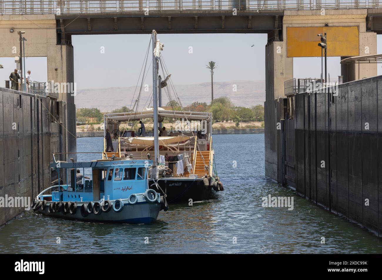 Un bateau à voile traditionnel dabahiya à deux mâts et son remorqueur entrent dans l'écluse d'Esna sur le Nil, en Égypte. Banque D'Images