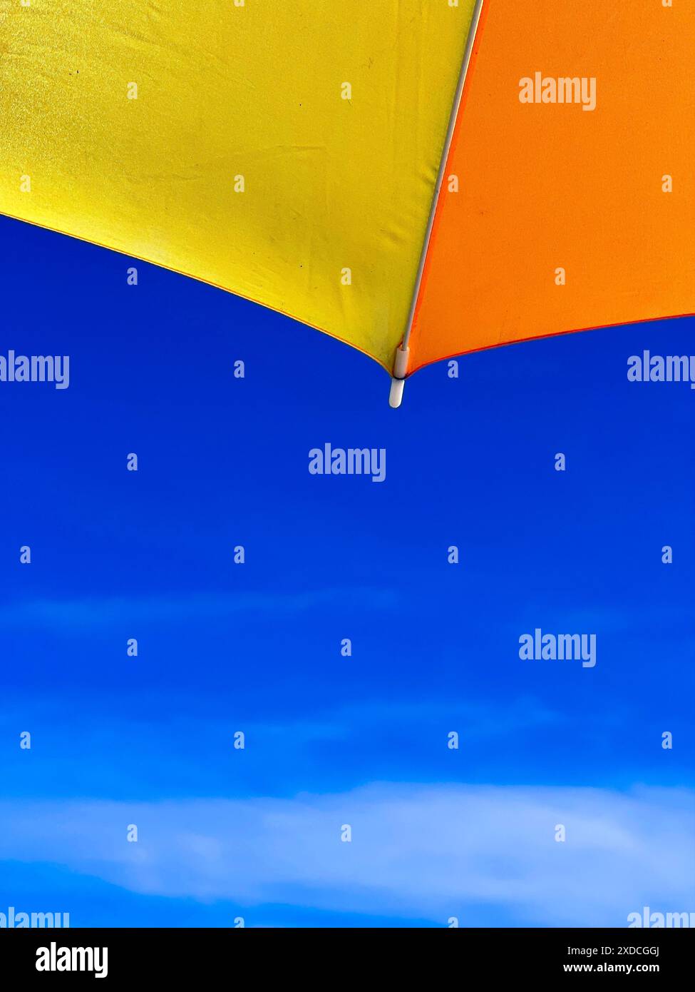 Gros plan d'un parasol jaune et orange vif contre un ciel bleu clair avec des nuages blancs tortueux. Le parapluie est positionné de telle sorte que seulement Banque D'Images