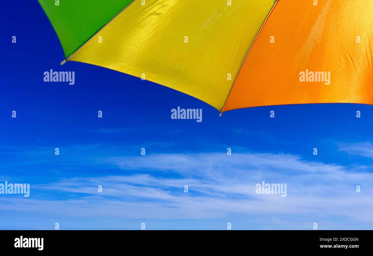 Gros plan d'un parasol jaune et orange vif contre un ciel bleu clair avec des nuages blancs tortueux. Le parapluie est positionné de telle sorte que seulement Banque D'Images