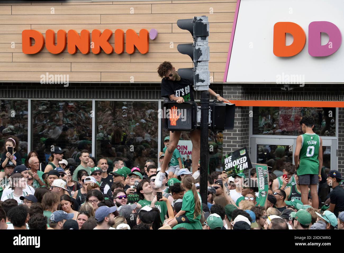 Boston, Massachusetts, États-Unis 21 juin 2024 Fan grimpant sur un feu de circulation devant un Dunkin Donuts avant le Boston Celtics Rolling Rally dans les rues de Boston pour célébrer les Celtics remportant la finale de la NBA pour la 18e fois. Plus d'un million de personnes ont longé la route du défilé pour encourager les Celtics à monter devant eux sur les Duck Boats. . (Rick Friedman) Banque D'Images