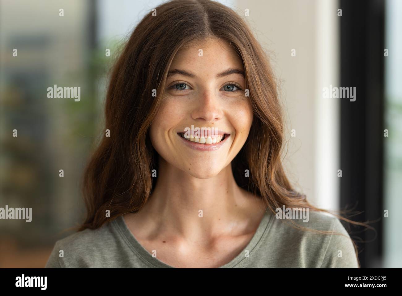 Femme souriante avec de longs cheveux bruns posant à l'intérieur, regardant la caméra Banque D'Images