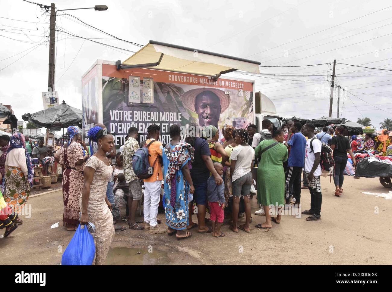 Residents line up in front of a mobile enrolment center from the Ivory Coast health authorities in Abidjan Monday, June 10, 2024. The country's universal health coverage program, has been criticized since its inception in 2019 for an inefficient voucher system that has made it impossible for participants to access the benefits. The mobile enrolment centers allow Ivorians to sign up for the scheme and provide them with cards on site, so that they can start receiving care immediately at hospitals, clinics, and pharmacies around the country. (AP Photo/ Diomande Ble Blonde) Banque D'Images
