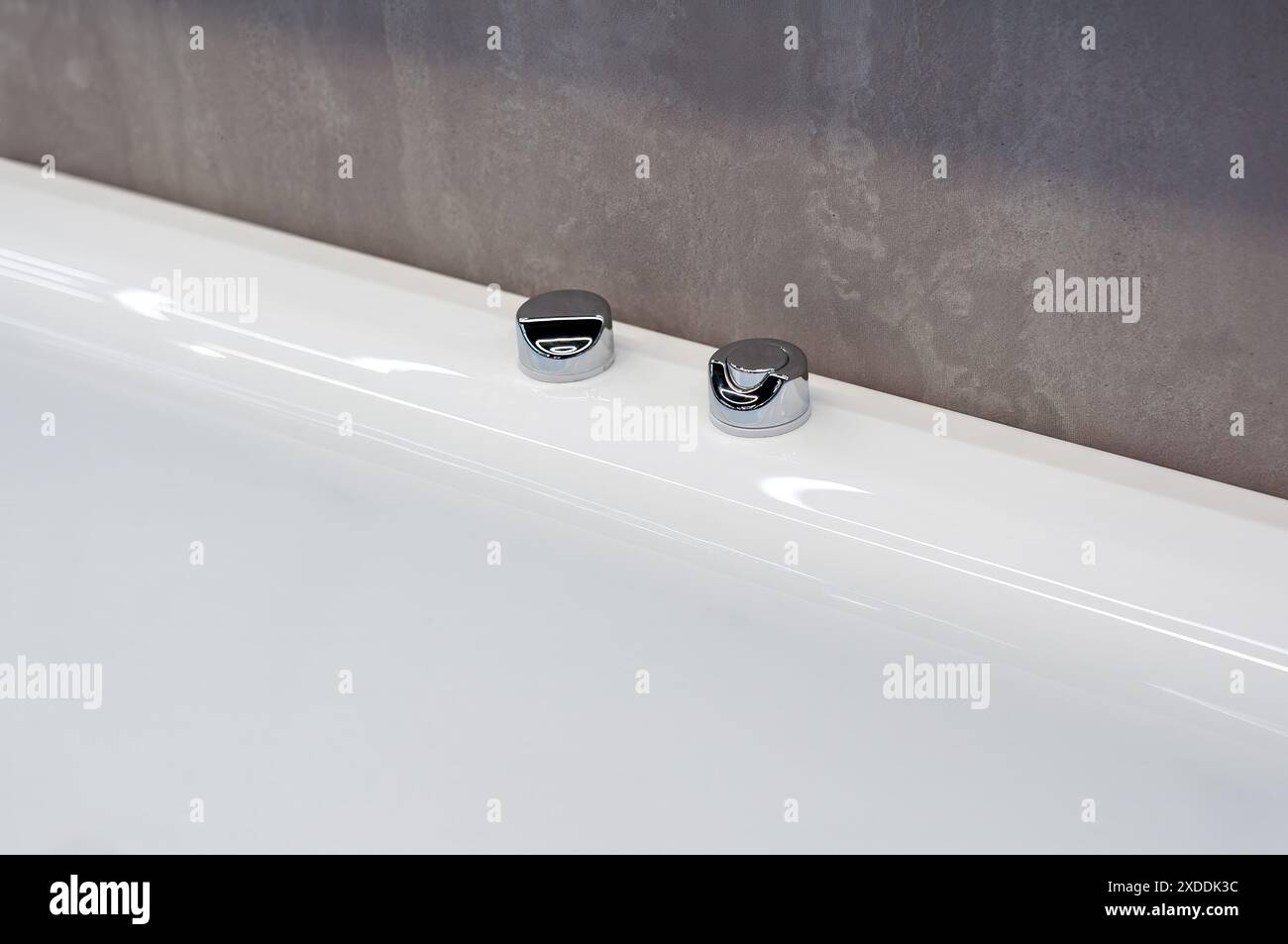 Deux couvercles chromés pour trous de robinet sur le bord d'une baignoire en acrylique dans une salle de bain moderne. Banque D'Images