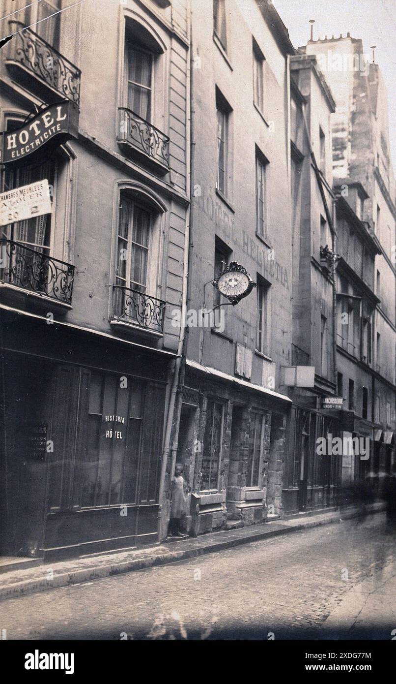 Photographie en noir et blanc d'une rue parisienne, montrant l'hôtel Helvtia au 41 rue de Montmorency. Ce bâtiment était autrefois la demeure de Nicolas Flamel, le célèbre alchimiste du XIVe siècle. La rue semble calme, avec quelques personnages visibles marchant le long des pavés. Banque D'Images