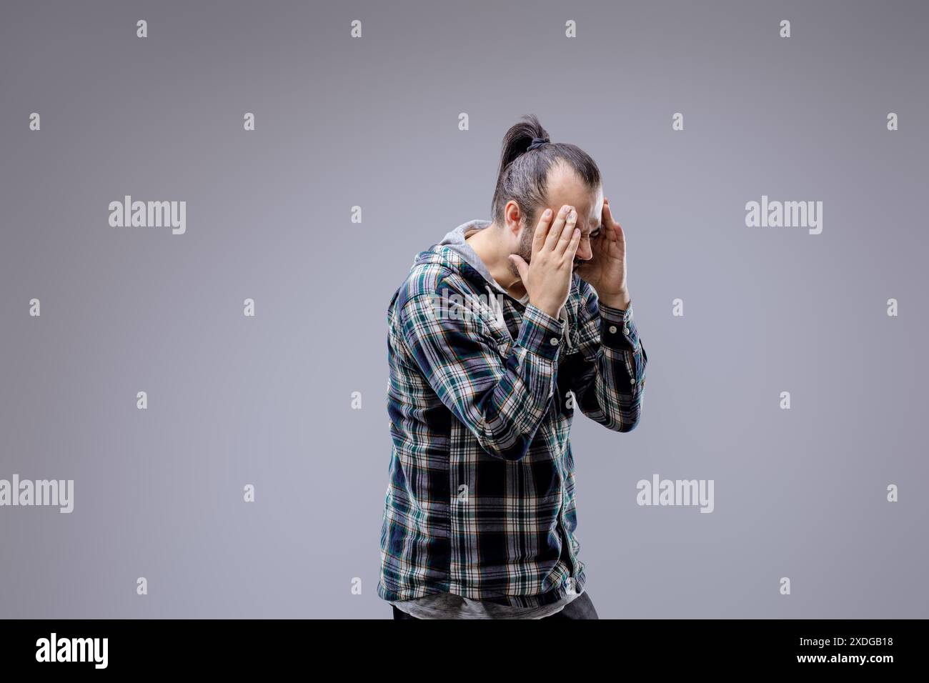 Le jeune homme lutte avec un mal de tête de tension, montrant douleur et stress. Il cherche soulagement et traitement pour ses souffrances Banque D'Images