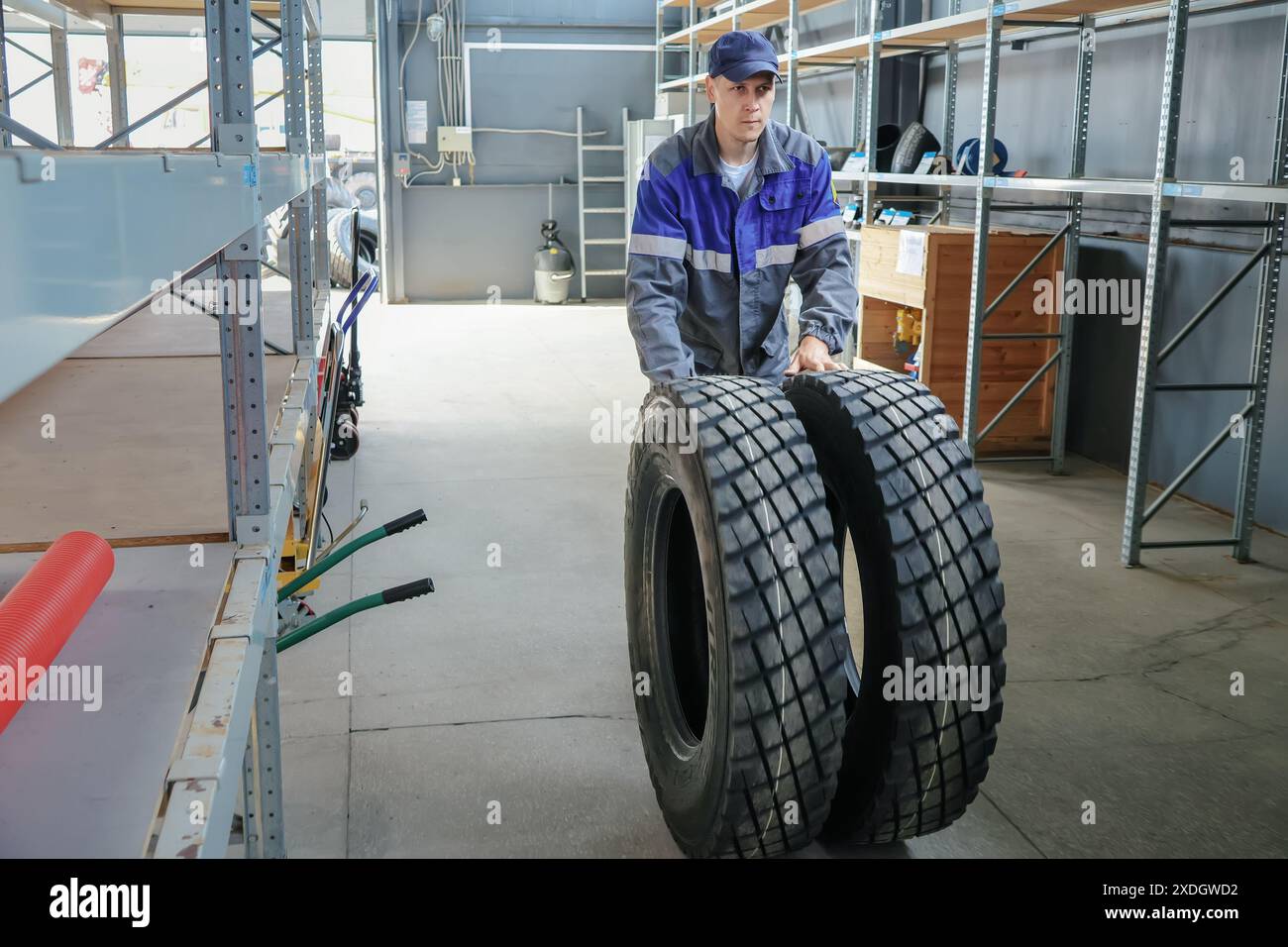 Un homme tient deux pneus dans un entrepôt. Les pneus sont noirs et sont sur une étagère Banque D'Images