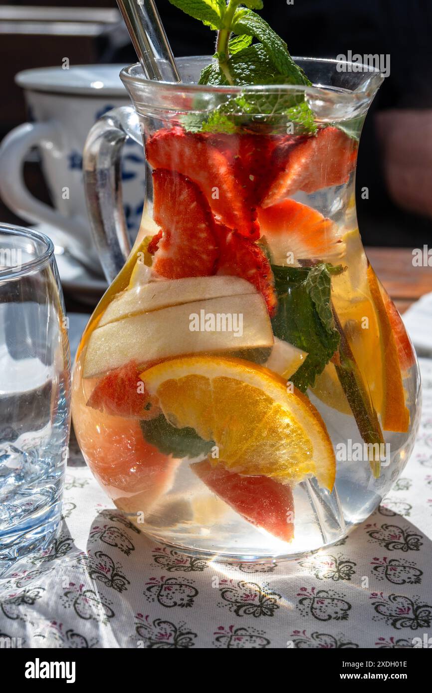 Beaucoup de fruits tranchés dans l'eau dans le pichet en verre, tasse et verre sur la table. Boisson vitaminée rafraîchissante en saison estivale. Banque D'Images
