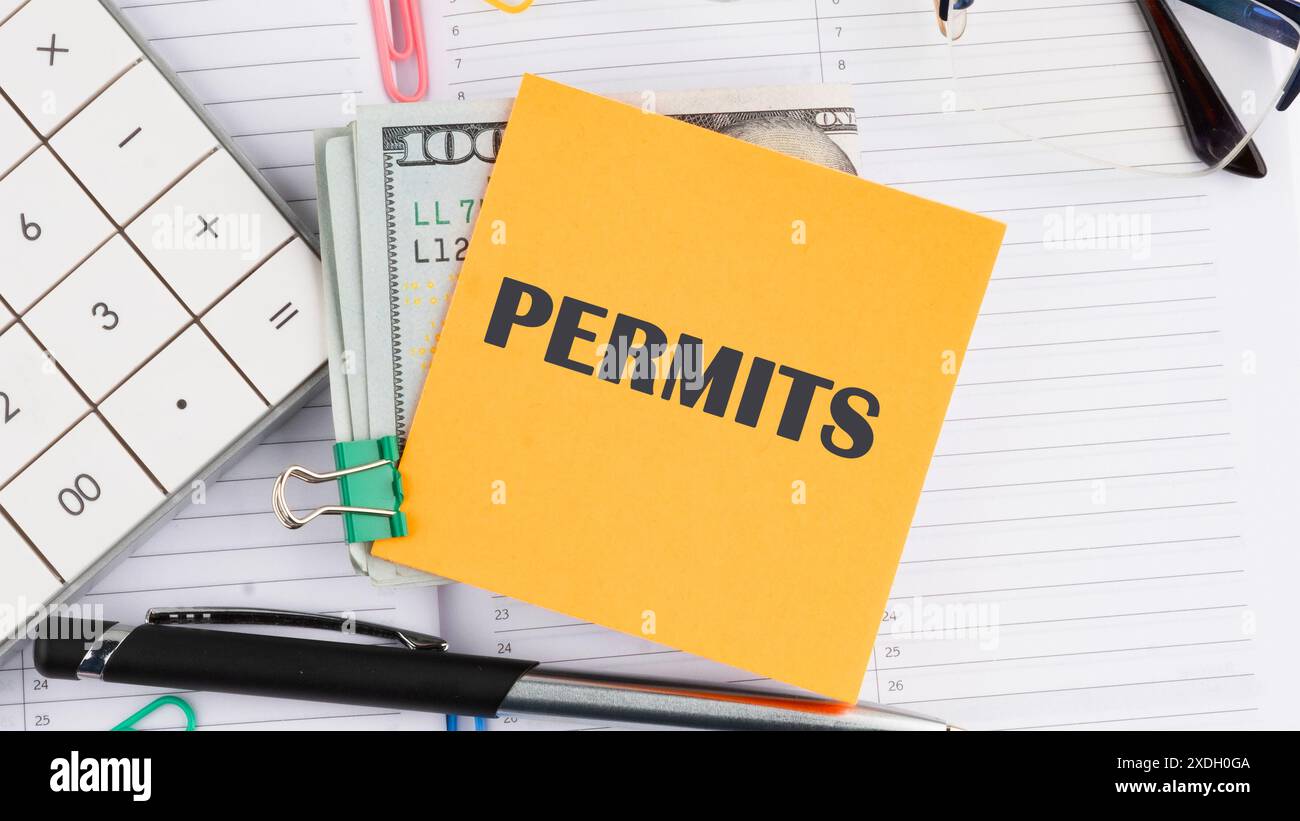 Concept d'affaires, mot de permis écrit sur un autocollant jaune à côté de billets de cent dollars américains, une calculatrice, un stylo sur un fond blanc Banque D'Images