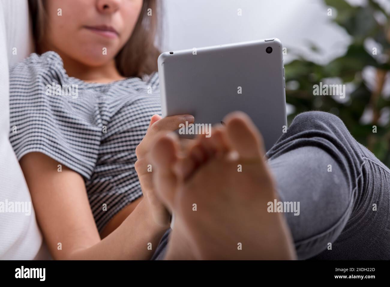 Jeune femme naviguant en ligne sur une tablette tout en se relaxant à la maison, immergée dans la technologie moderne pour les loisirs et la communication Banque D'Images