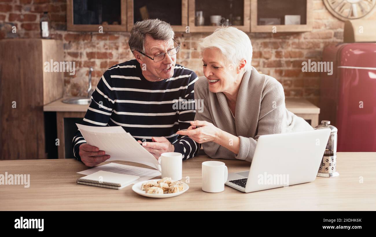 Couple senior examinant les documents ensemble dans la cuisine Banque D'Images