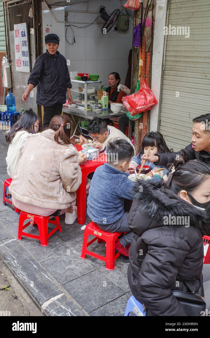 Hanoi, Vietnam - 9 février 2024 : les dîners sont assis à manger à un stand de nourriture de rue dans le vieux quartier de Hanoi Banque D'Images