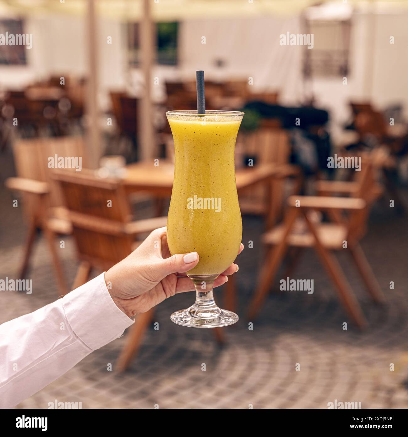 Serveuse tenant un smoothie rafraîchissant aux fruits tropicaux par une chaude journée d'été dans un café en plein air Banque D'Images