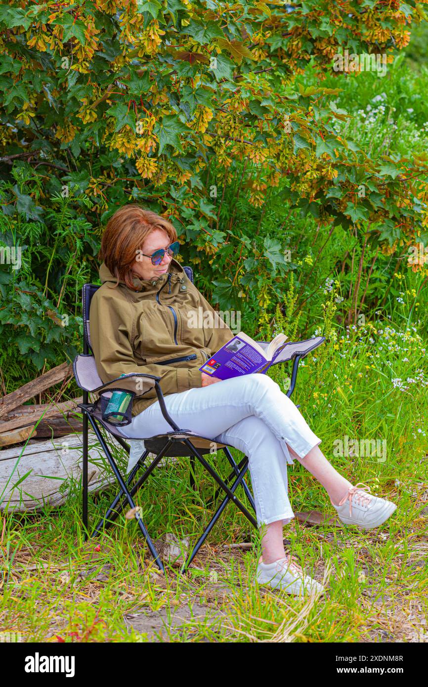 Belle grand-mère assise lisant un livre près du fleuve Fraser près de Vancouver Canada Banque D'Images