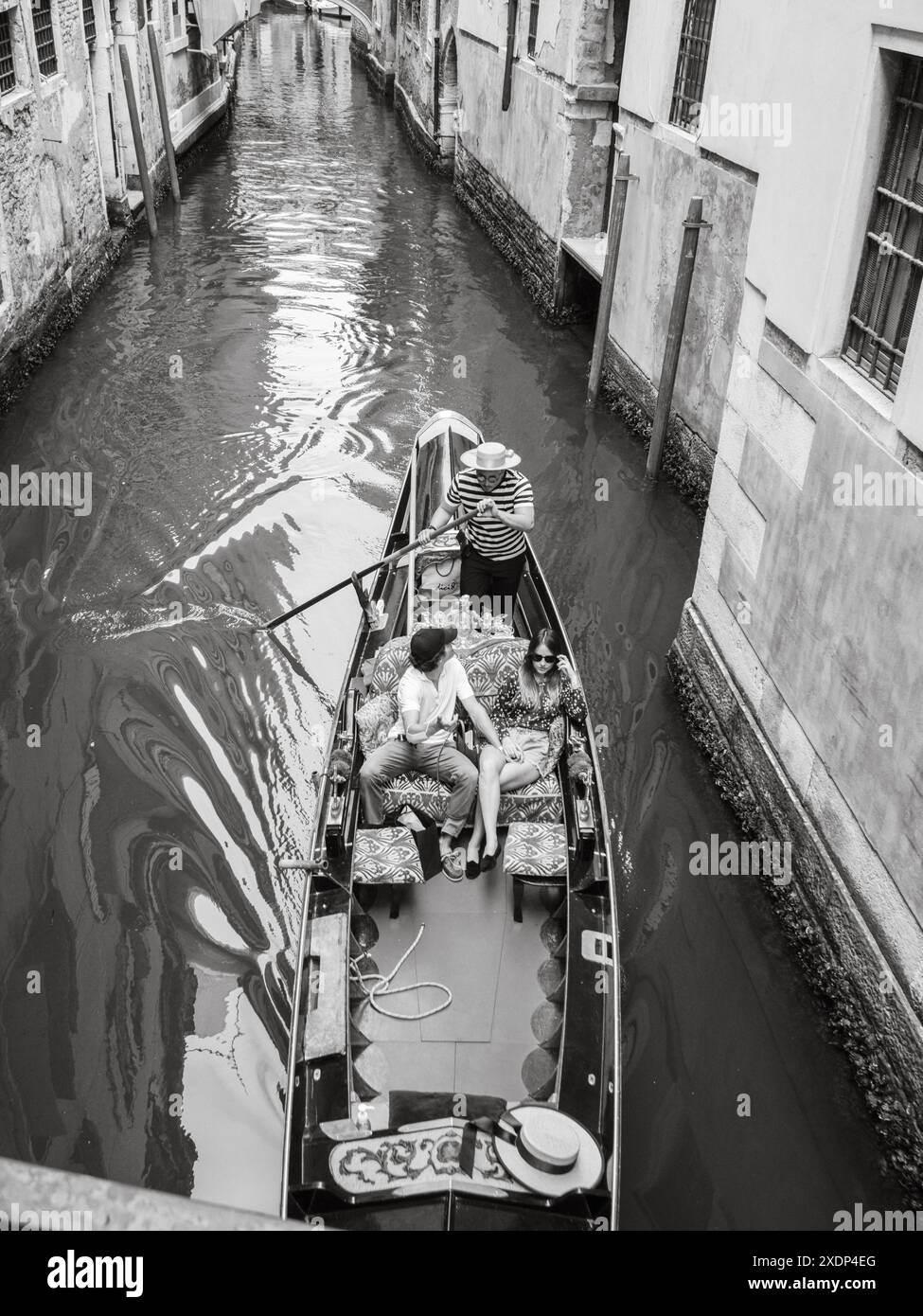 Venise, Italie - 30 juin 20220 le gondolier utilise une longue rame pour propulser une gondole à travers un étroit canal à venise, tandis qu'un couple est assis dans le b. Banque D'Images