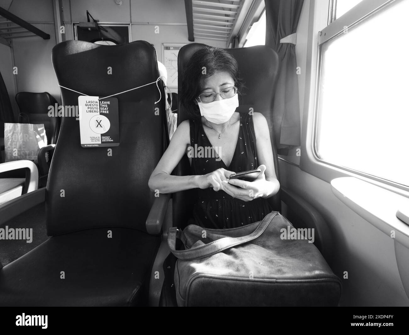 Venise, Italie - 30 juin 20220 femme utilise son smartphone en train, portant un masque protecteur et assise à côté d'un siège vide w Banque D'Images