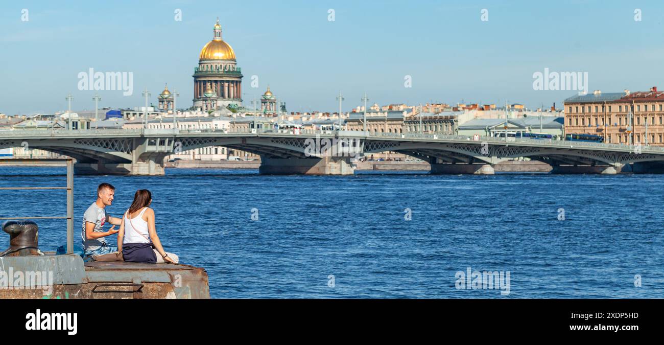 Saint-Pétersbourg, Russie - 28 juin 2018 : jeune couple assis à la jetée de la rivière Neva avec la cathédrale Isaakievsky sur le fond, photo panoramique Banque D'Images