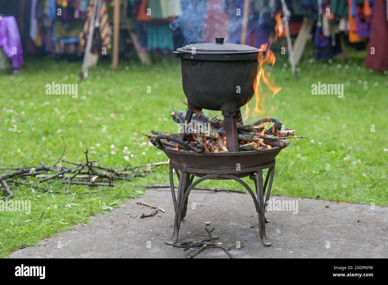 Brasier de feu avec bois brûlant et une marmite de cuisine en fer à trois pieds pour préparer un repas à l'extérieur sur un marché médiéval, espace copie, foyer sélectionné, étroit Banque D'Images
