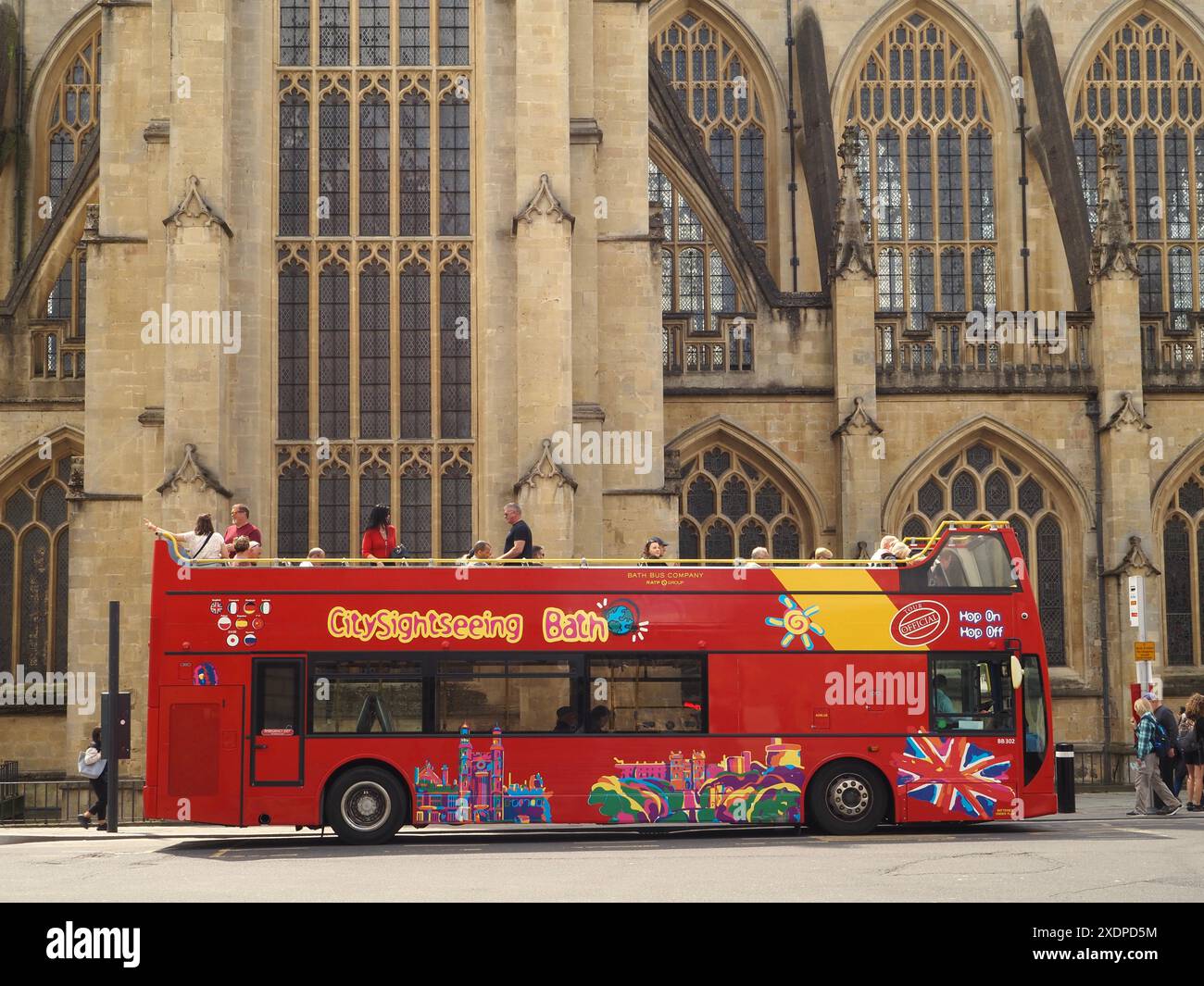 Bus Toot bus à arrêts multiples pour visites guidées de la ville à toit ouvert avec des personnes qui montent et descendent du bus, et abbaye de Bath en arrière-plan. Bath, Somerset, Royaume-Uni Banque D'Images