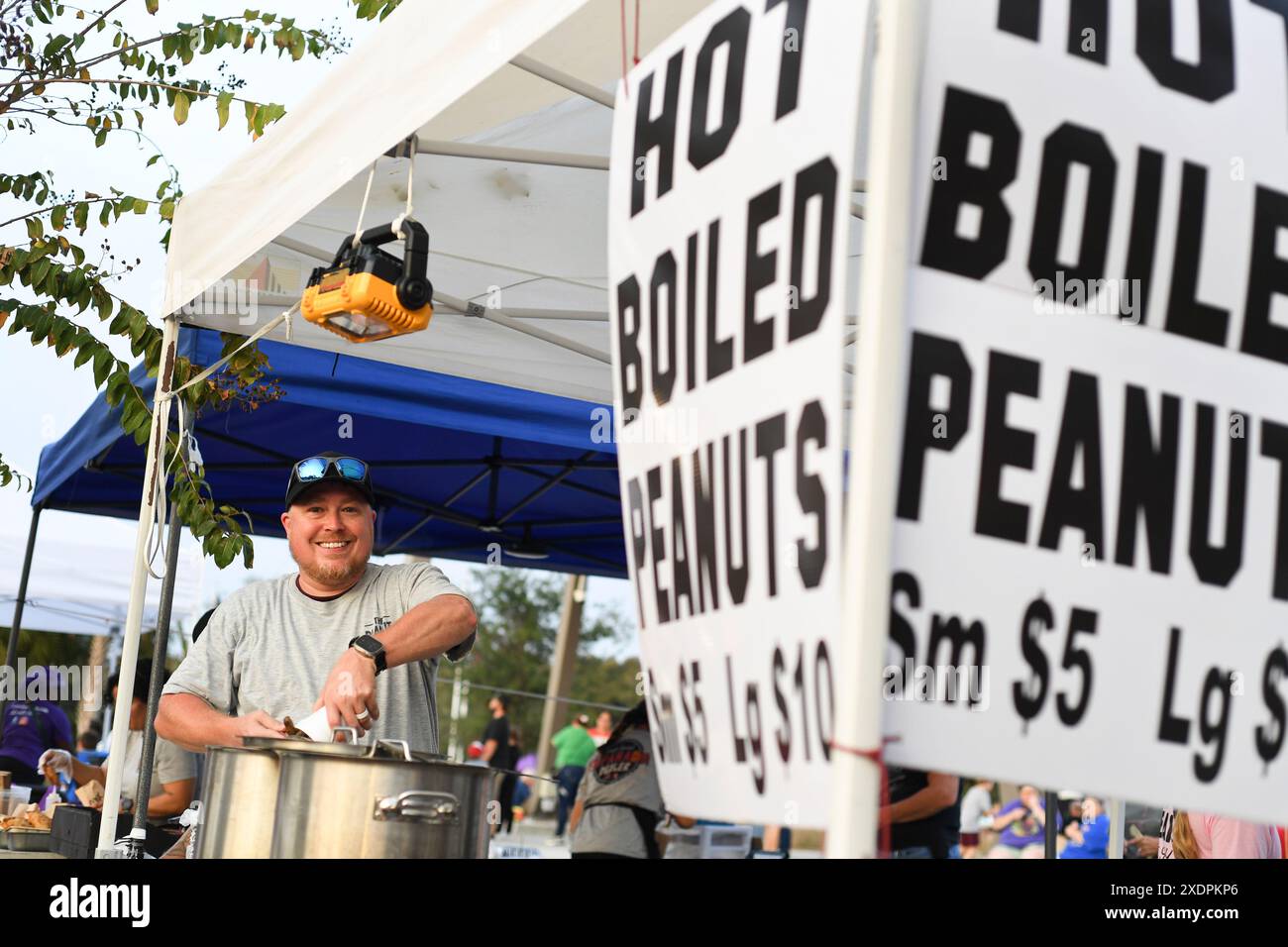 Vendeur souriant vendant des cacahuètes bouillies chaudes sur un marché en plein air. Banque D'Images