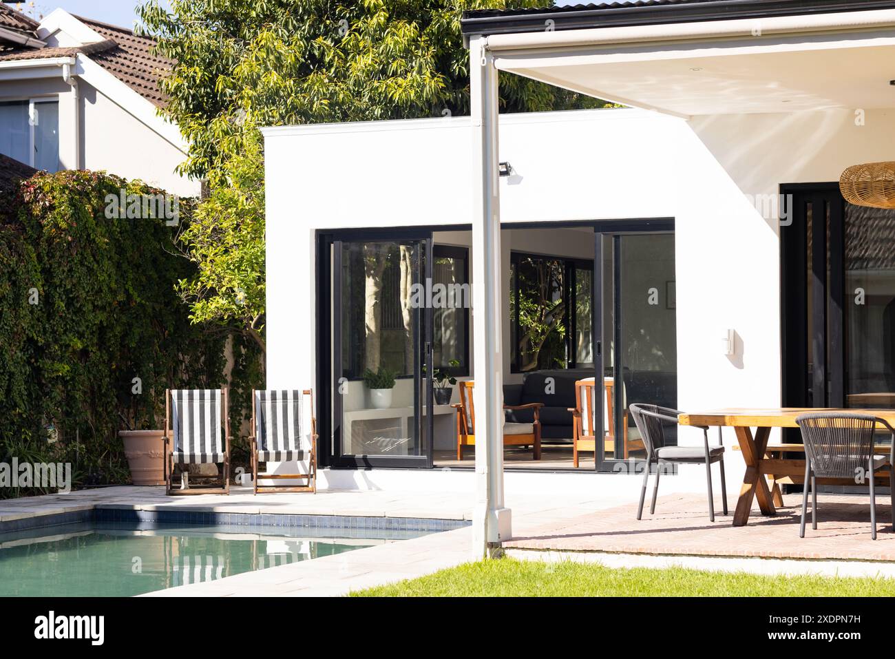 Jardin moderne avec piscine, chaises longues et salle à manger extérieure par temps ensoleillé, espace photocopie Banque D'Images