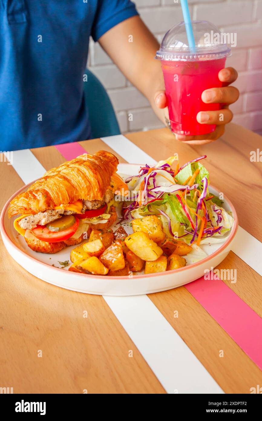 Homme portant une chemise bleue tenant la boisson de glace de baies mangeant croissants sandwich poulet nourriture de style de vie. Banque D'Images