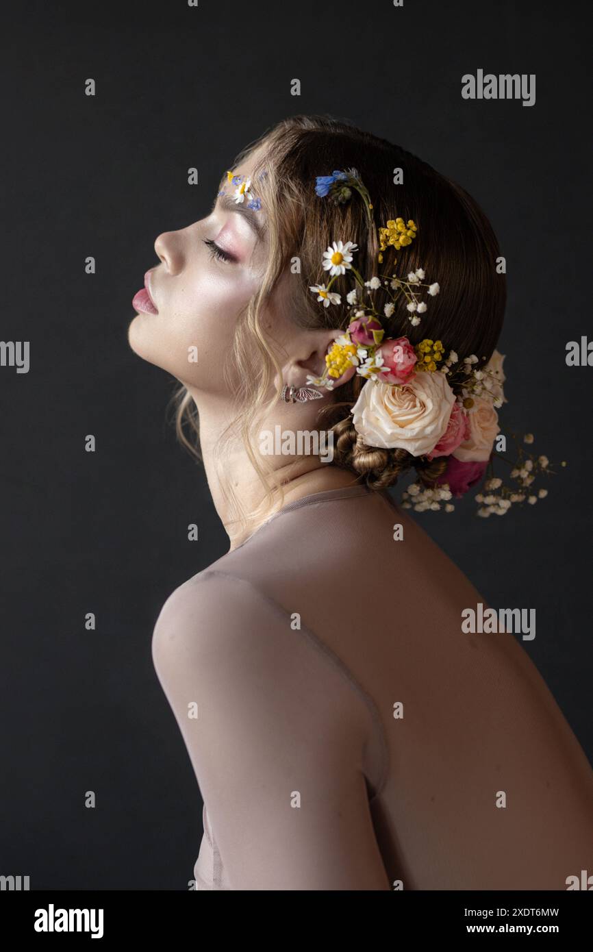 Une femme avec une couronne florale et maquillage est photographiée dans un cadre de studio, son profil capturé les yeux fermés. L'éclairage et la composition cr Banque D'Images
