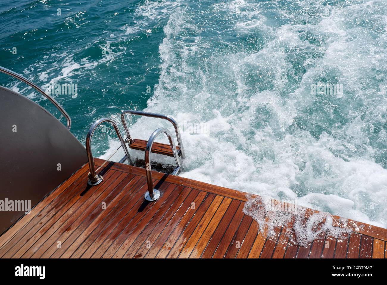 Pont arrière en bois de teck et échelle métallique d'un yacht à moteur, vagues et éclaboussures de mer et mousse. Banque D'Images