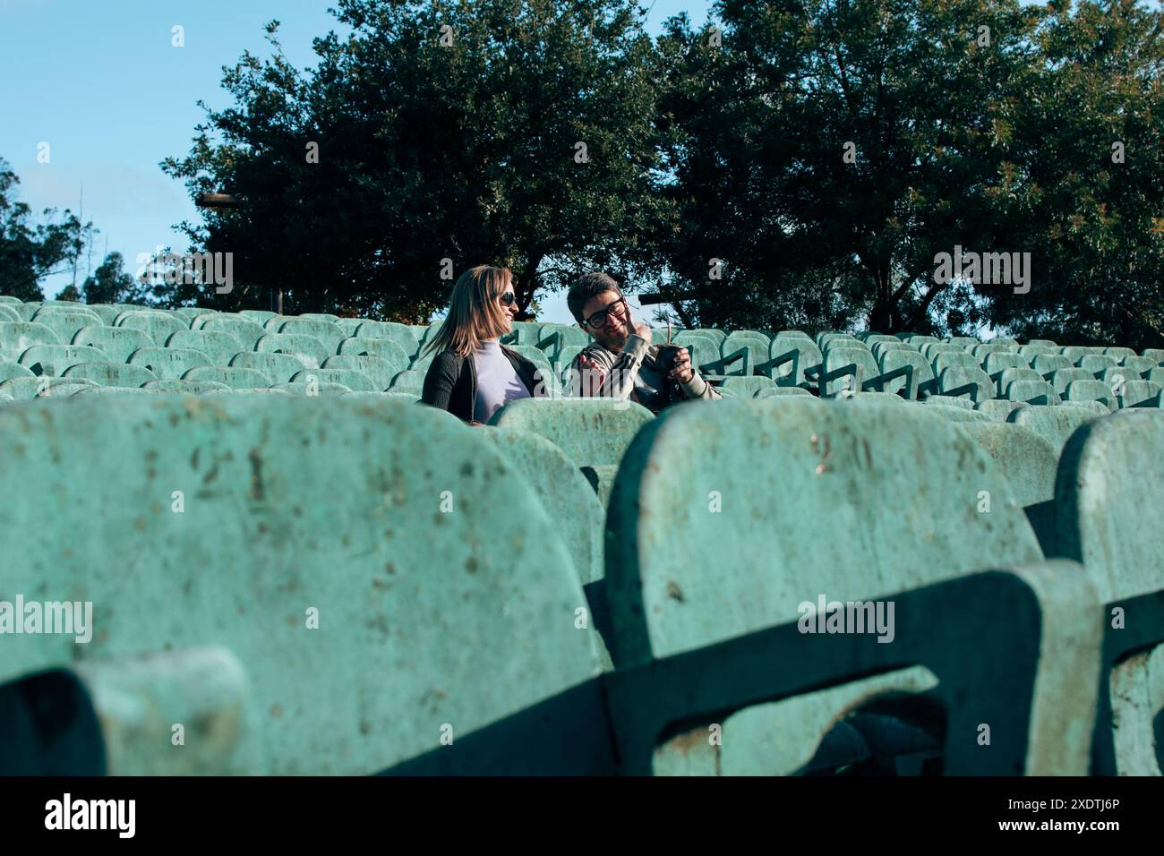 Deux visiteurs sont assis parmi des rangées de sièges turquoise usés dans un amphithéâtre en plein air à Lapataia, Uruguay, par une journée ensoleillée. Banque D'Images